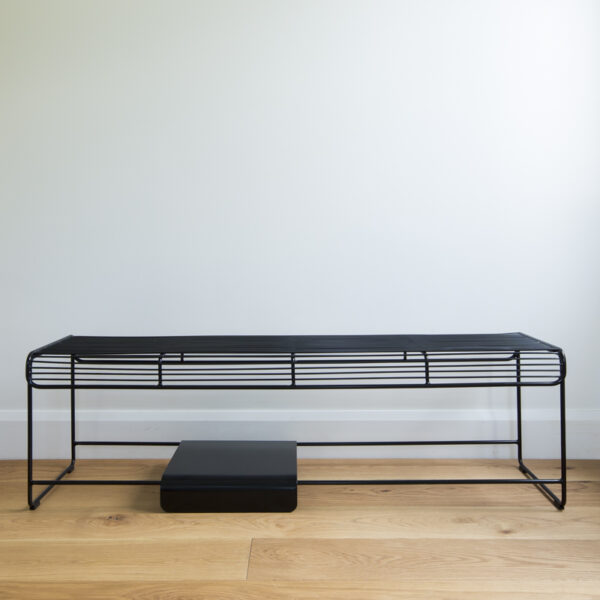 Black wire bench seat with a movable solid metal plate sitting on the bottom rungs